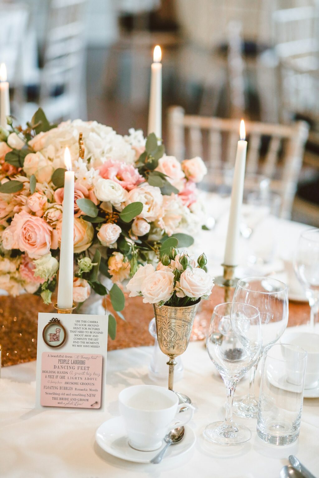 Elegant wedding centrepiece with floral arrangement, candles and an invitation card displayed on a banquet table